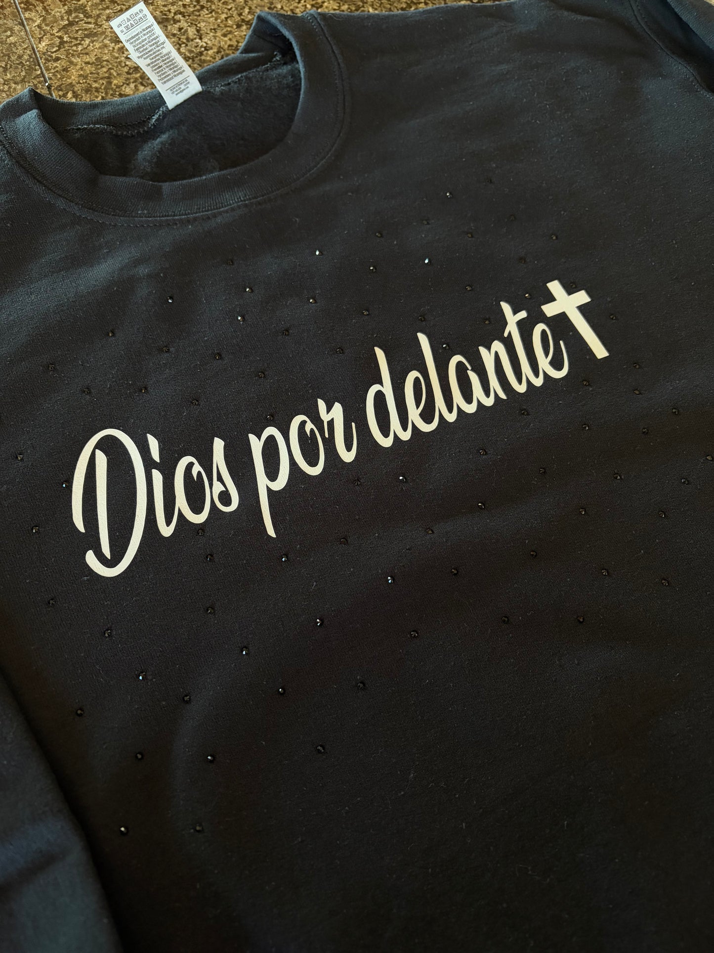 Black sweatshirt, with white text 'Dios por delante' with black scattered rhinestones around the white text, closer look